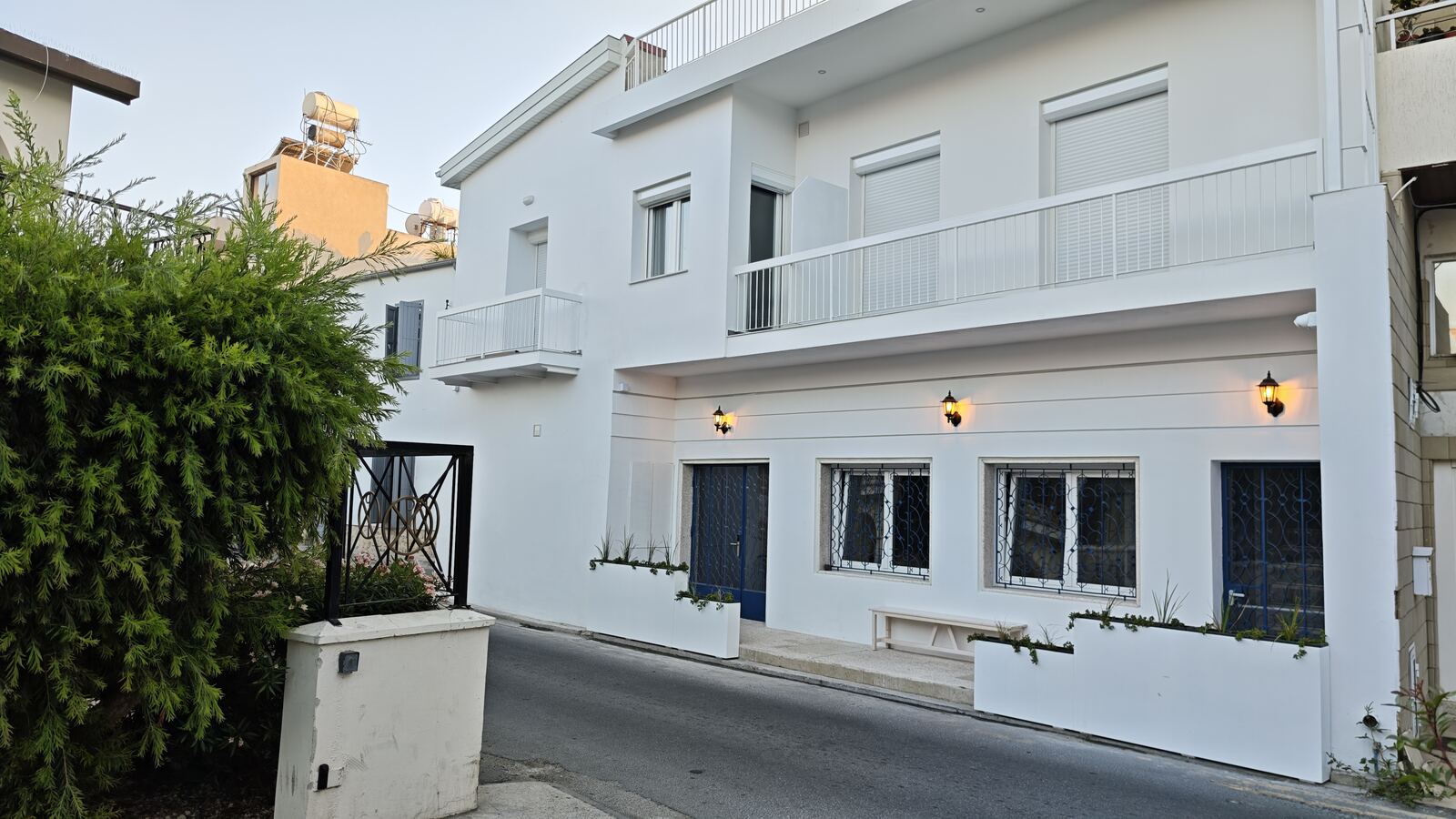 St. Lazarus City Hotel exterior at dusk, whitewashed facade with cobalt blue window grilles, Larnaca old town