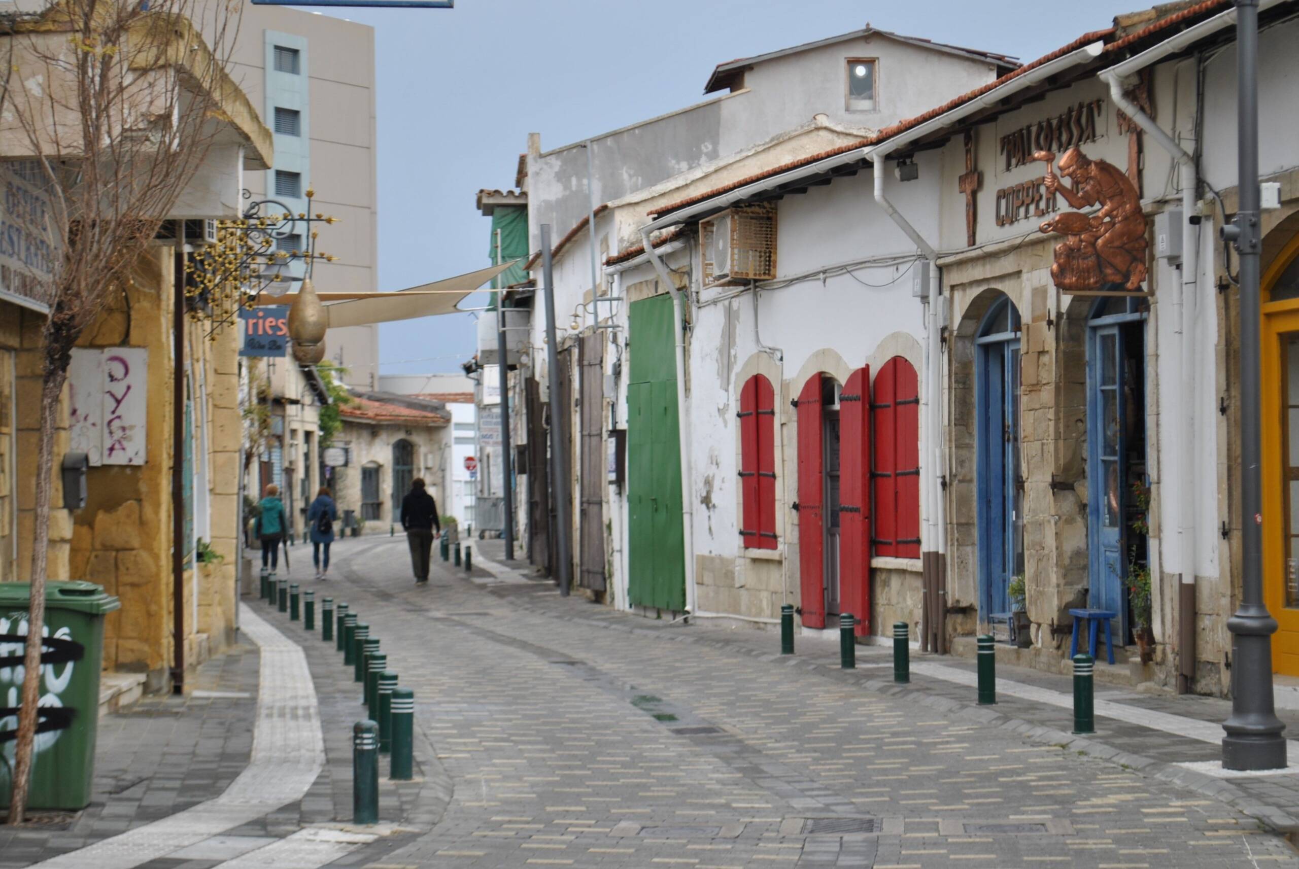A quiet old street in Larnaca with red shutters and a coppersmith's sign